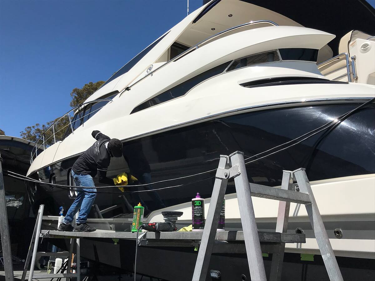 Detailer polishing the dark hull of a large motor yacht on the hardstand