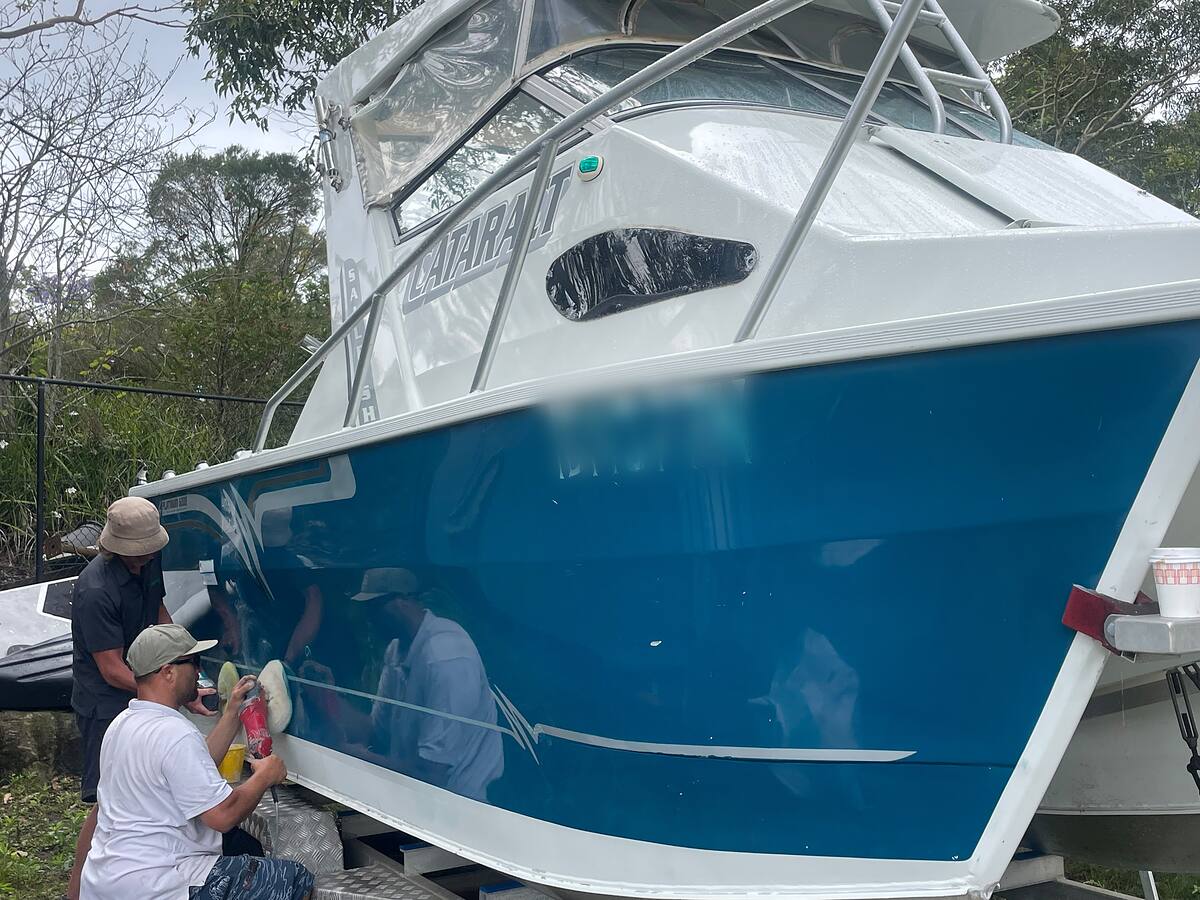 Two detailers machine polishing the blue hull of a Cataract trailer boat