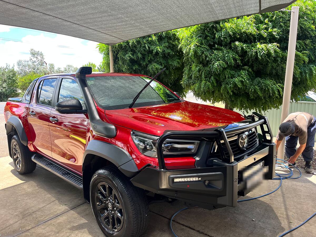 Red Toyota HiLux gleaming after a mobile detail, detailer packing up the hose