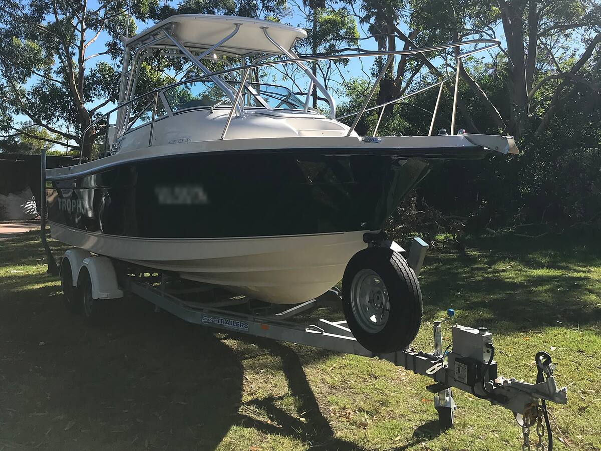 Trailer boat with a gloss black hull and hardtop on its tandem trailer, ready for detailing